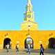 A picture of the the city gate of Cartagena de Indias in Columbia, with a bright yellow wall and a spire rising over it.